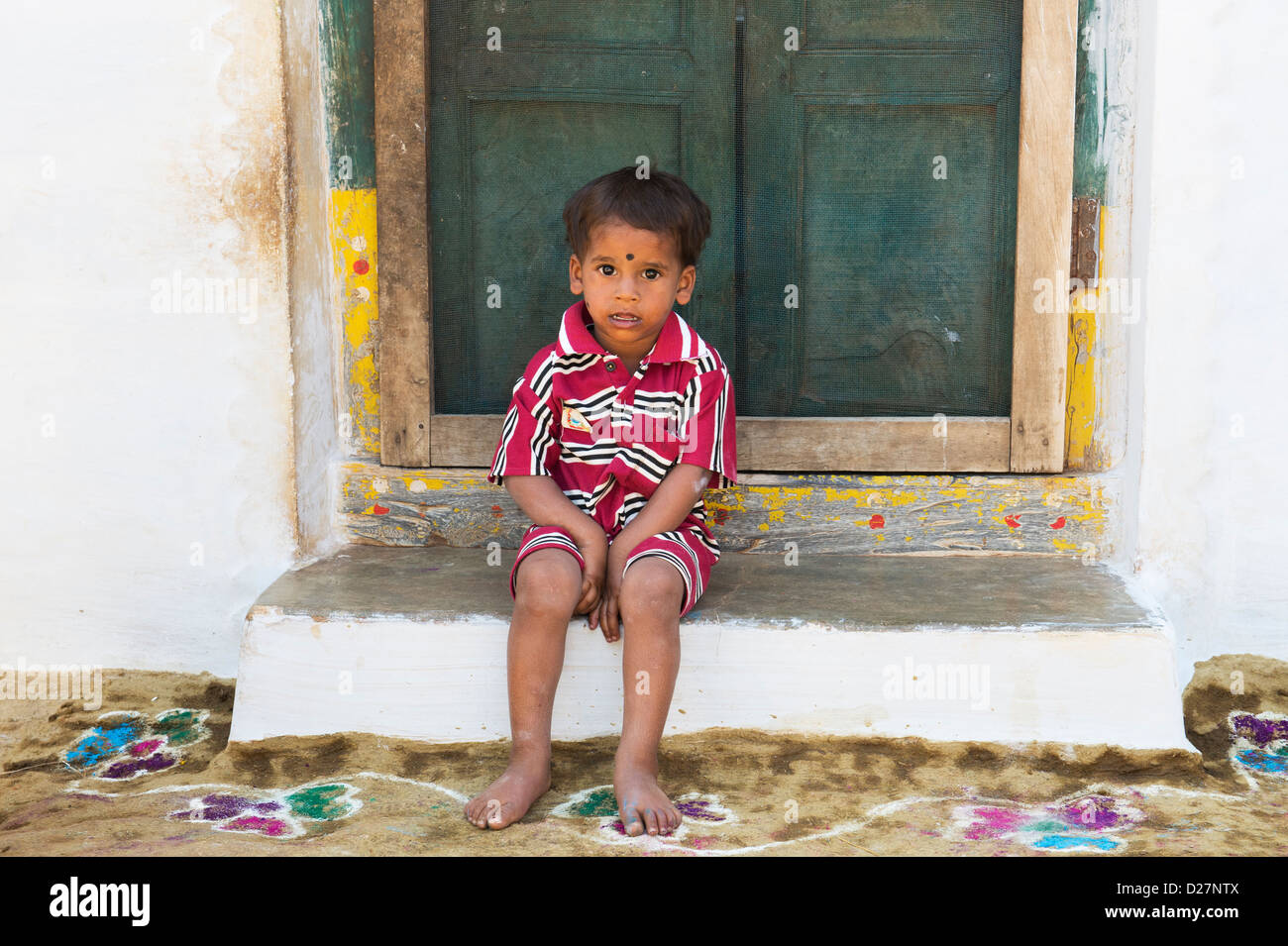 Village indien jeune garçon assis sur le seuil de son domicile. L'Andhra Pradesh, Inde Banque D'Images