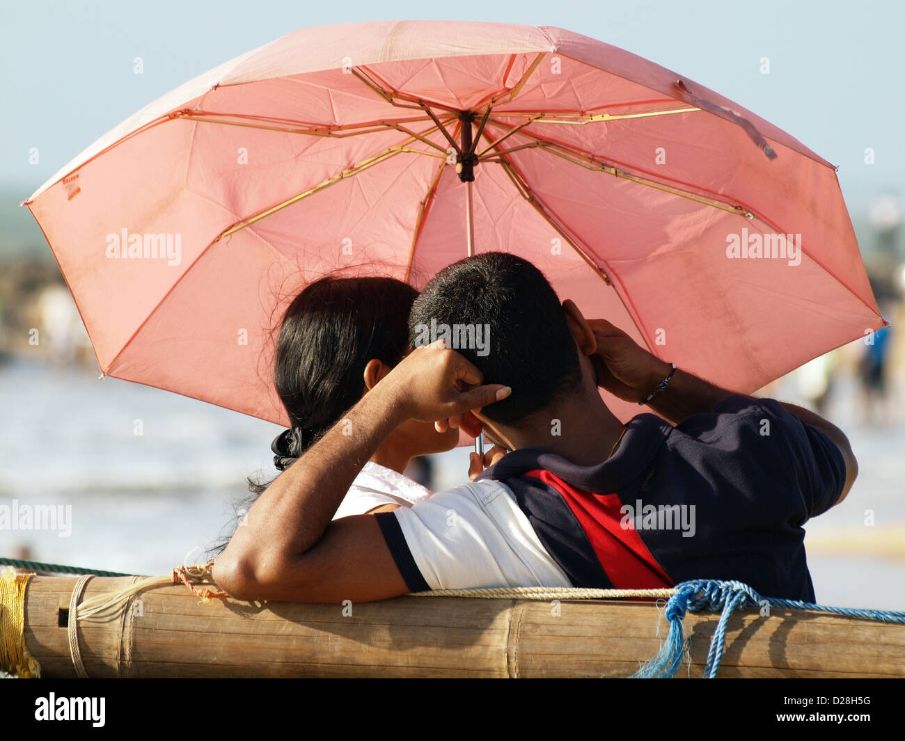 Un jeune couple à la recherche d'intimité sur la plage au Sri Lanka l'abri sous un parasol comme ils aiment la compagnie des autres Banque D'Images