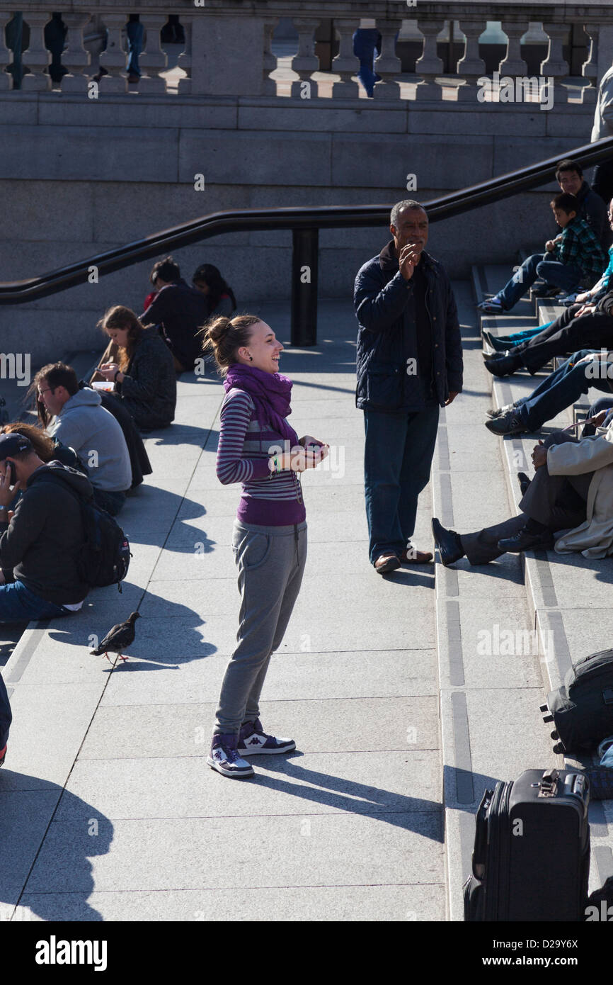 Touriste rit alors qu'elle s'apprête à photographier ses amis à Trafalgar Square, Londres. Banque D'Images