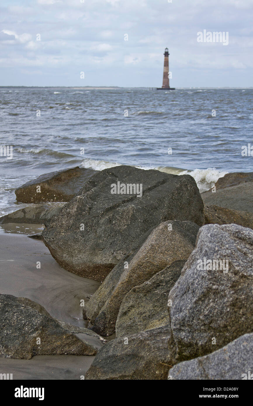 Morris lointain phare au large de la côte de la Caroline du Sud avec surf et rochers en premier plan Banque D'Images