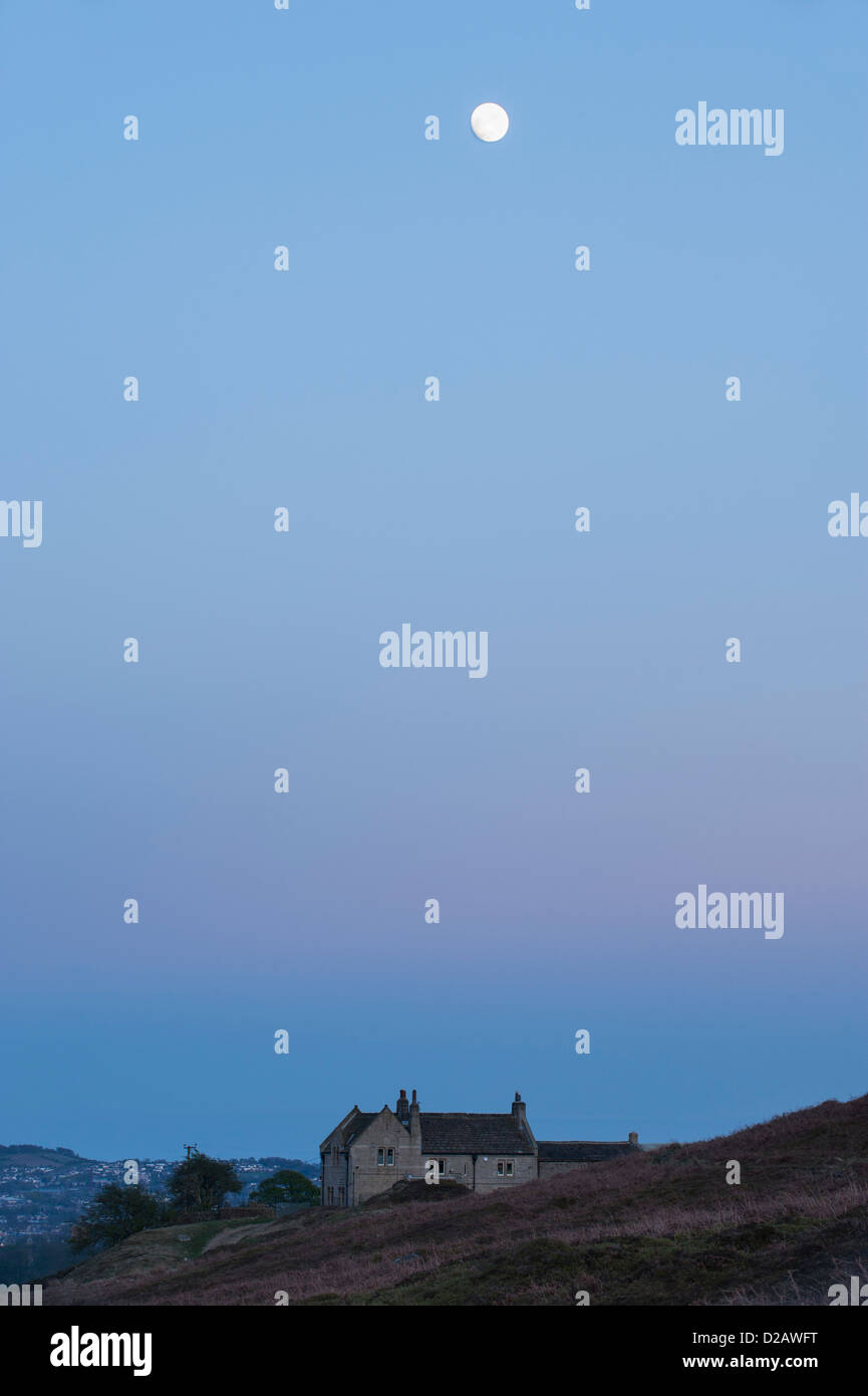 Pleine lune au crépuscule, haut dans un ciel bleu au-dessus sur une maison en pierre sur la lande de bruyère - au-dessus de Burley-en-Wharfedale, West Yorkshire, Angleterre, Royaume-Uni. Banque D'Images