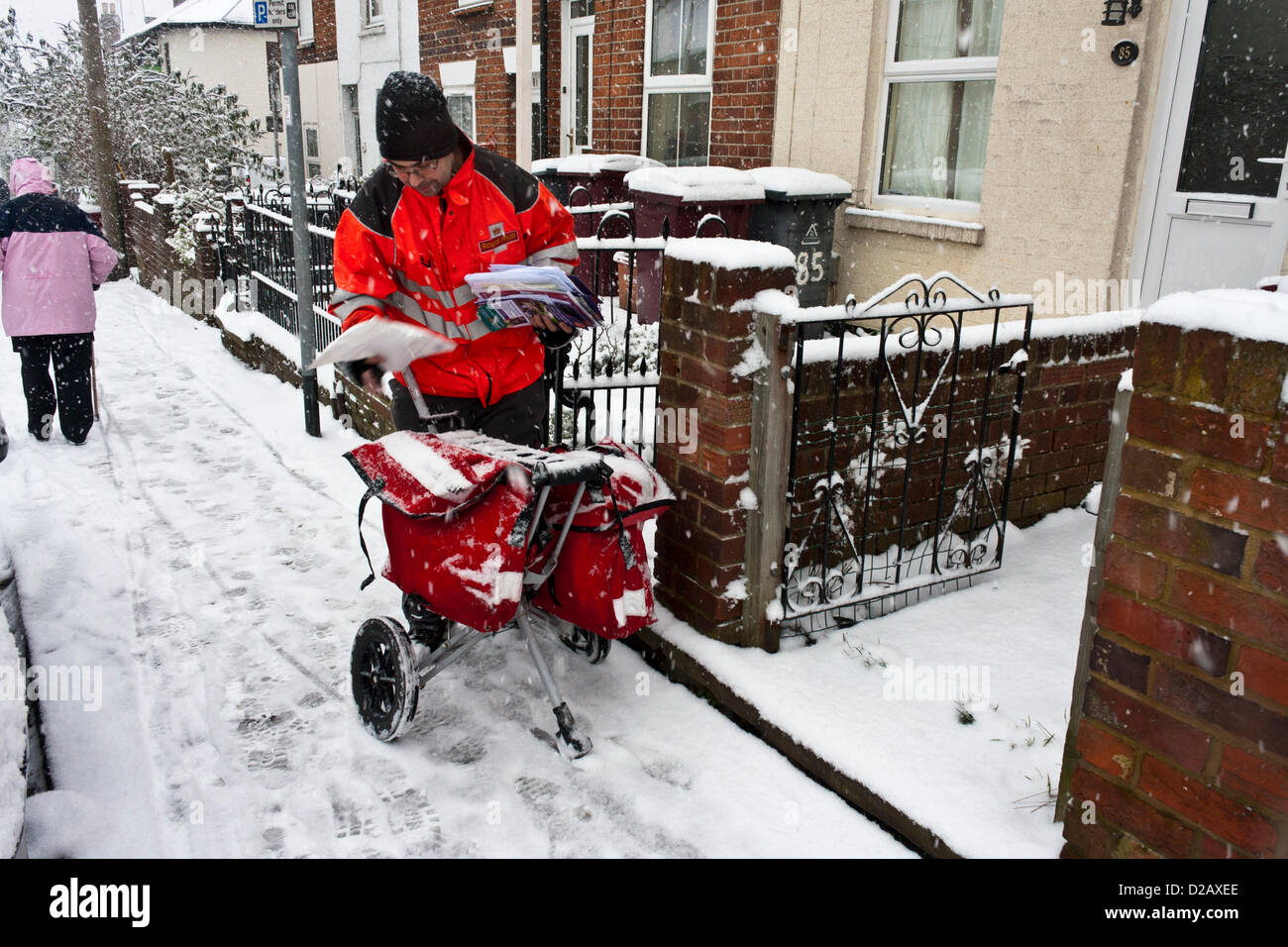 Royal Mail postman offre mail en temps d'hiver neigeux, tandis qu'une femme âgée, escaliers à travers la glace aux pieds. Reading, Berkshire, Angleterre, Royaume-Uni. Banque D'Images