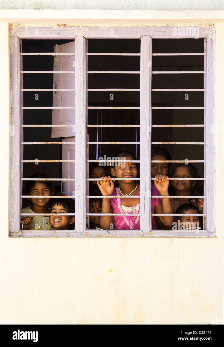 Les jeunes enfants du village indien à la fenêtre à travers les barreaux d'une maison indienne. L'Andhra Pradesh, Inde Banque D'Images