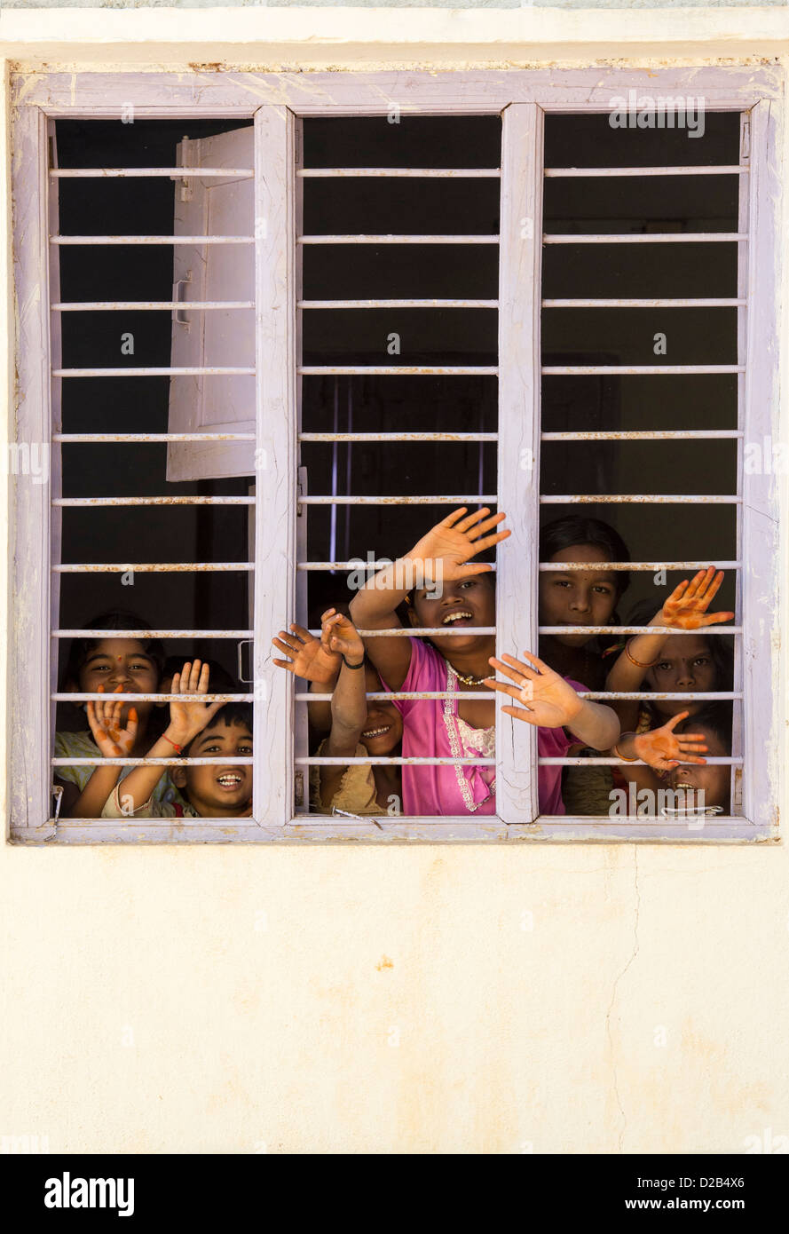Les jeunes enfants du village indien à la fenêtre à travers les barreaux d'une maison indienne. L'Andhra Pradesh, Inde Banque D'Images