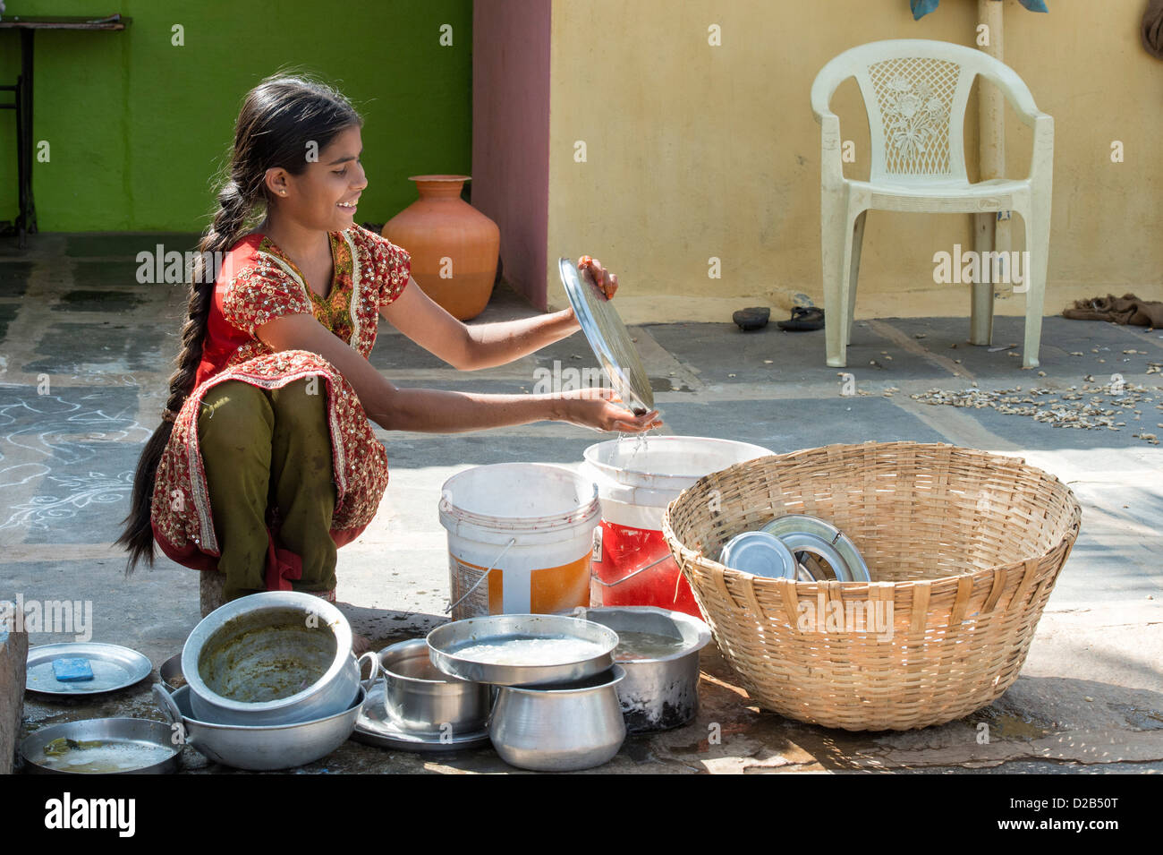 Teenage Indian girl lave-vaisselle à l'extérieur de son village de l'Inde rurale accueil. L'Andhra Pradesh, Inde Banque D'Images