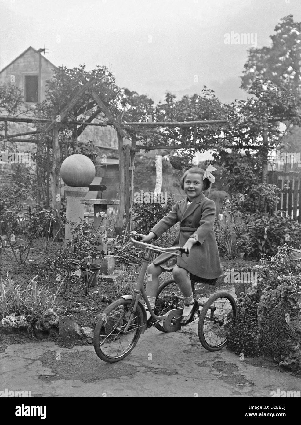Fille jouant sur son tricycle dans un jardin, ch. 1950 Banque D'Images