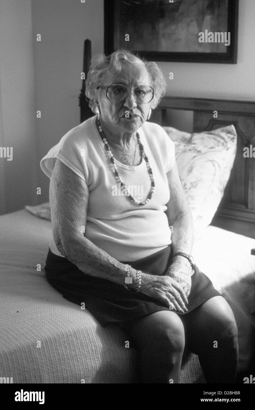 Femme âgée assise sur un lit, portant des lunettes Banque D'Images