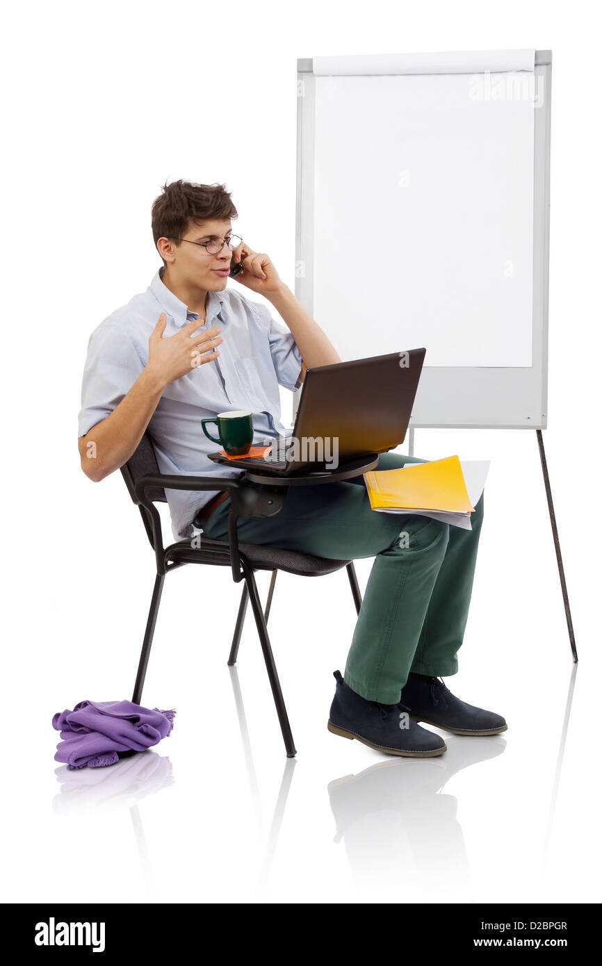 Jeune homme avec des lunettes s'exprimant sur mobile et de travail sur l'ordinateur portable dans un milieu de travail Banque D'Images