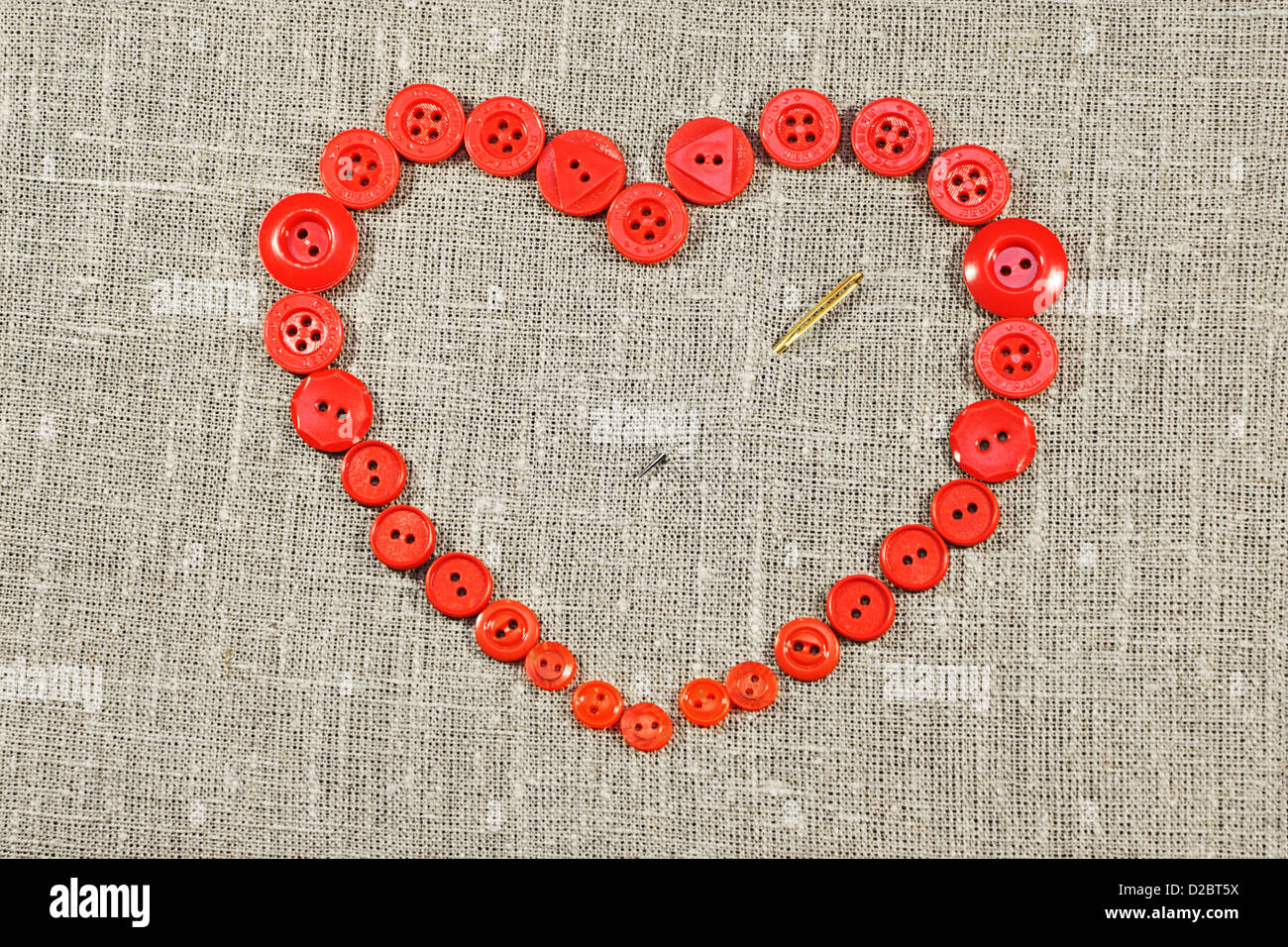 Coeur en forme de boutons rouges de l'aiguille percée. Objet sur tissu écru. Banque D'Images