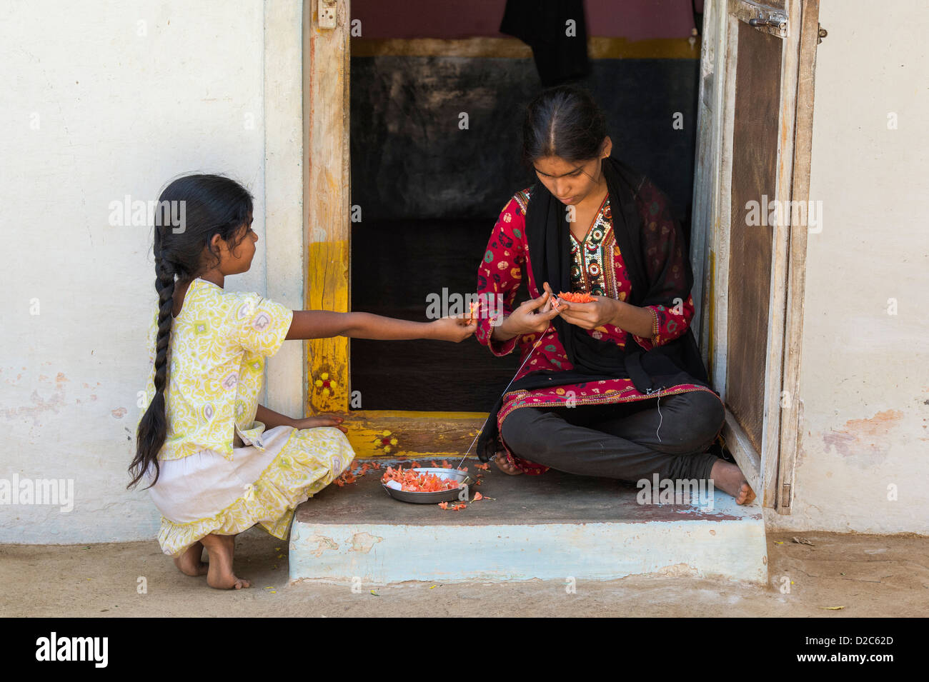 Les filles indiennes faisant une guirlande de fleurs à l'extérieur d'une maison de village. L'Andhra Pradesh, Inde Banque D'Images