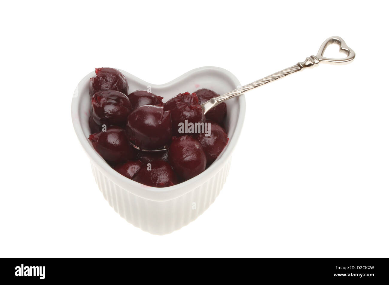 Conserves de cerises noires en forme de coeur dans un ramequin avec une cuillère isolés contre white Banque D'Images