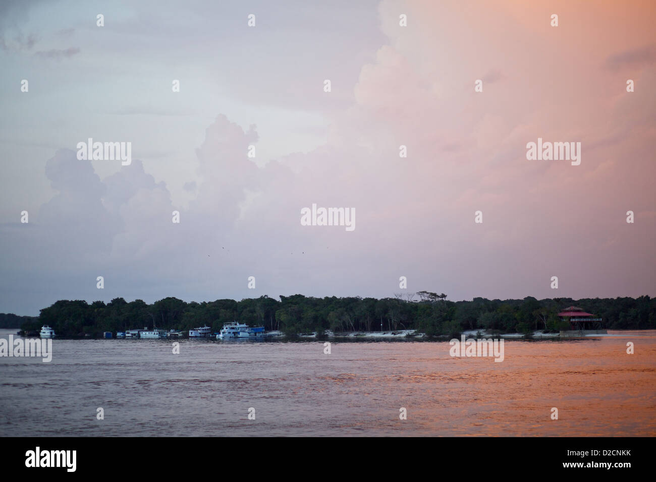 Vue sur le coucher du soleil d'une communauté riveraine sur la rivière Amazone au Brésil, avec des bateaux amarrés, et une voie navigable tranquille sous un ciel coloré Banque D'Images