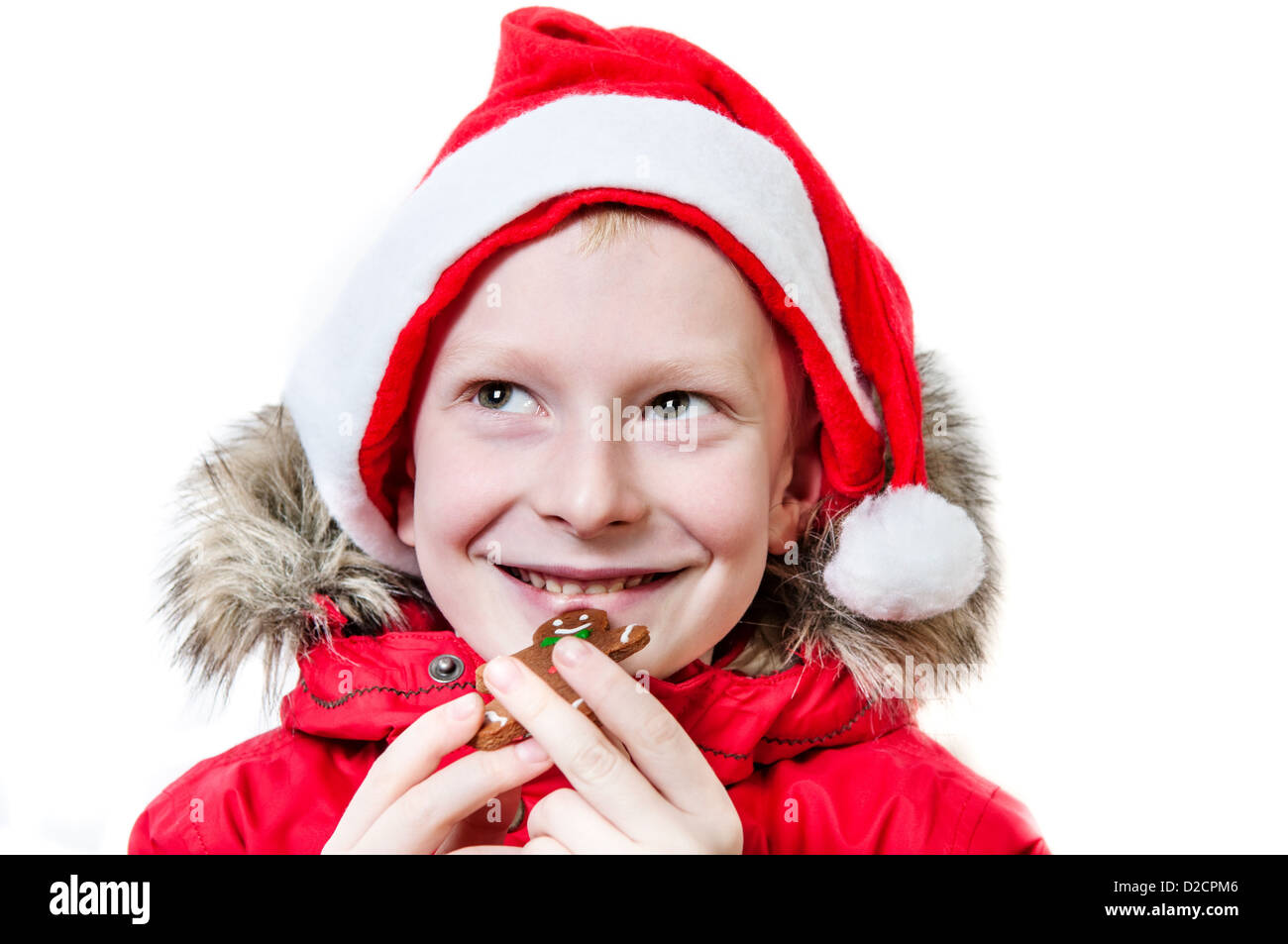 Smiling boy wearing santa hat eating gingerbread man. Banque D'Images