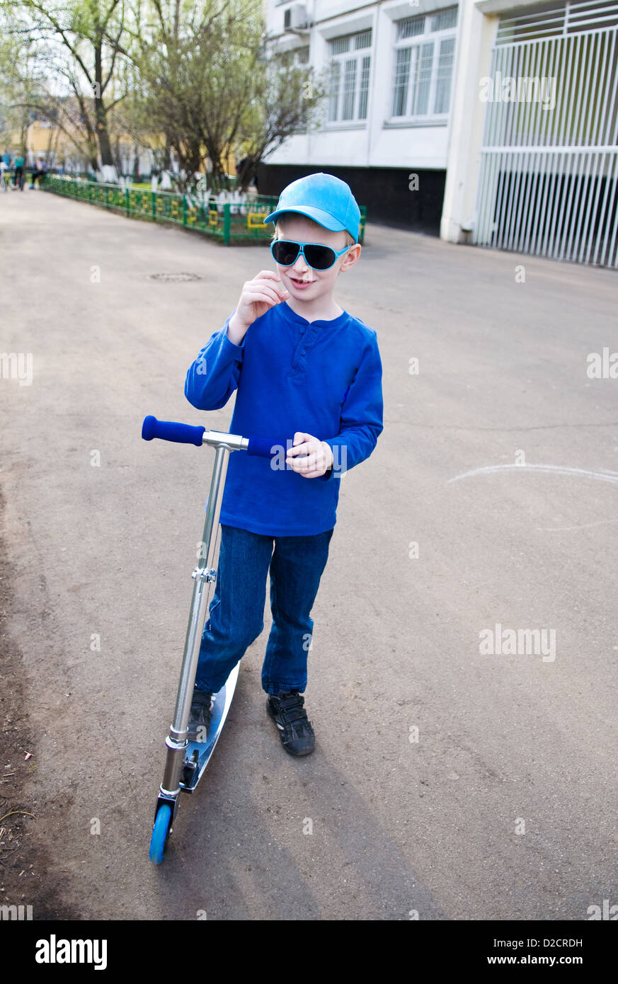 Cute smiling boy wearing sunglasses riding scooter Banque D'Images