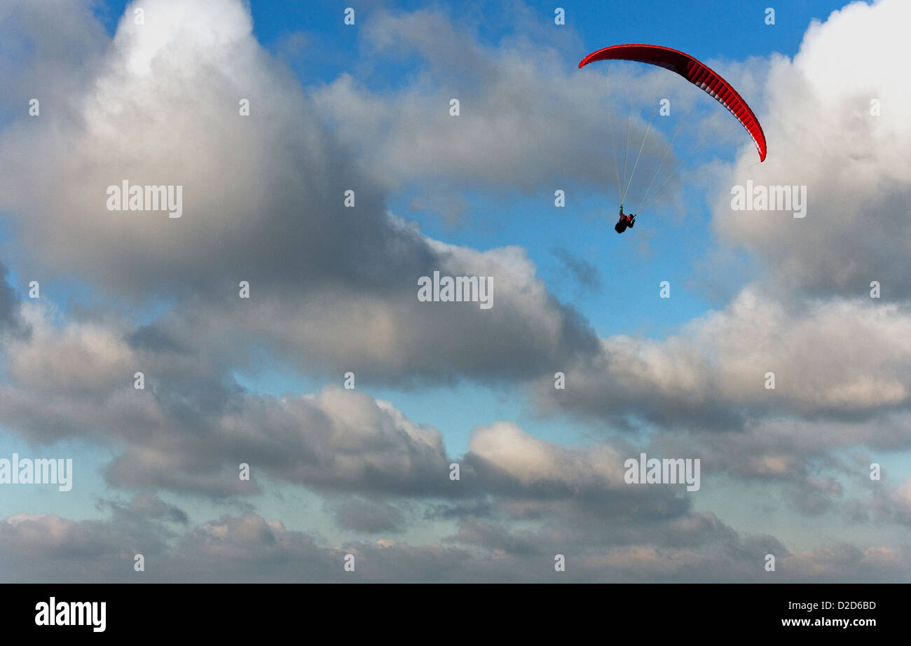 Un homme vole en parapente sur le Sud des bas dans le West Sussex avec une chute rouge sur un beau jour avec ciel bleu et nuages blancs Banque D'Images