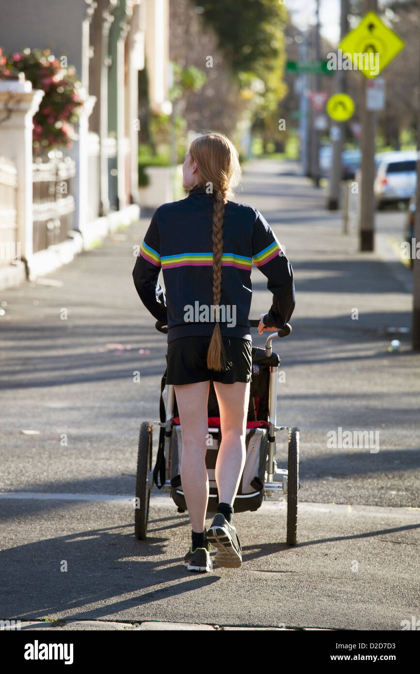 Vue arrière d'une femme marchant sur un trottoir avec un landau Banque D'Images