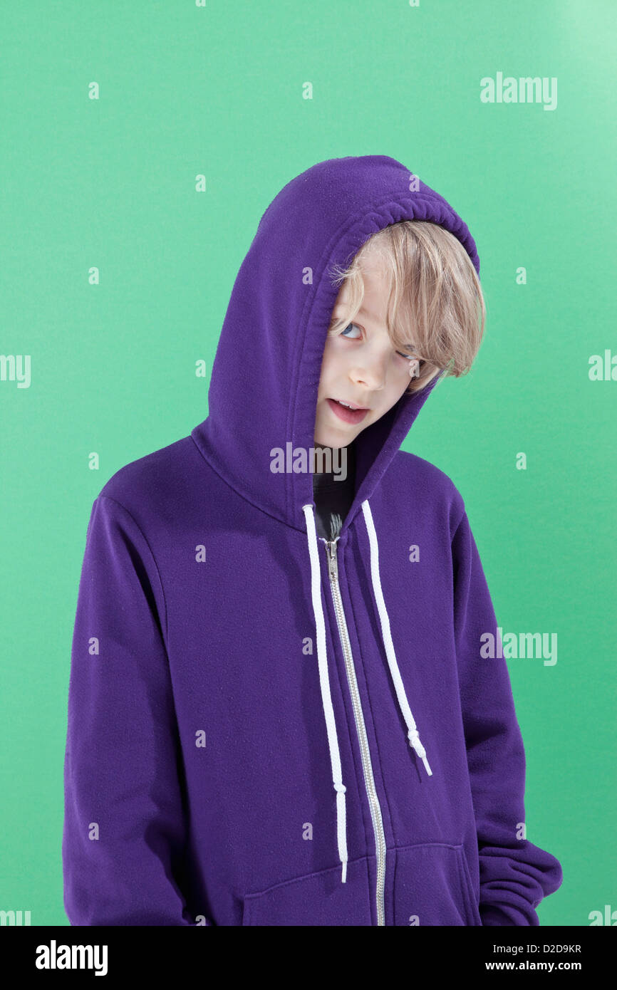 Un garçon avec le capot de son sweatshirt up peeking timidement à l'appareil photo Banque D'Images