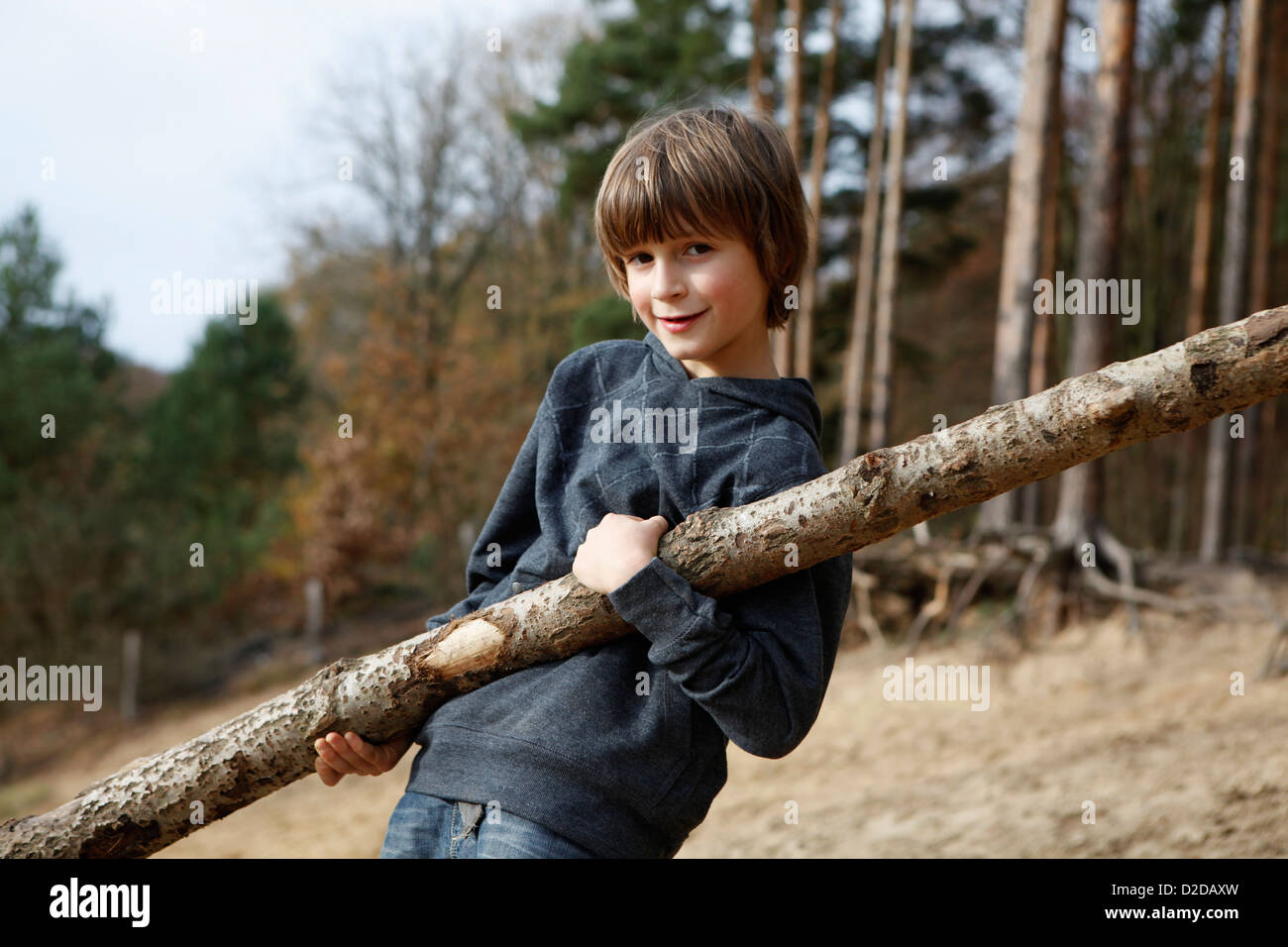 Un garçon porteur d'une grande branche dans une région boisée Banque D'Images