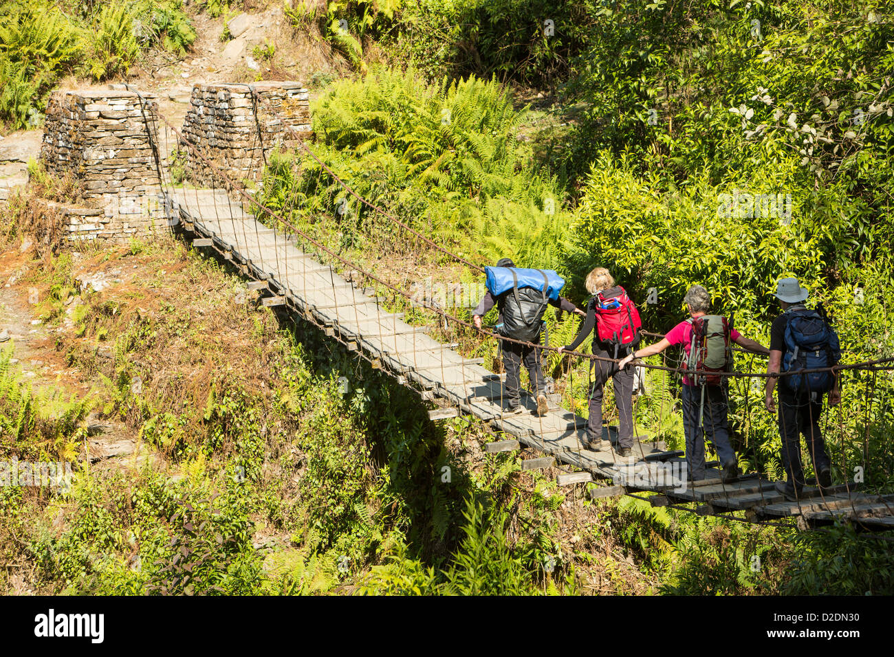 Randonneurs traversant un pont suspendu sur le passage du Camp de base de l'Annapurna, trek Himalaya, Népal. Banque D'Images