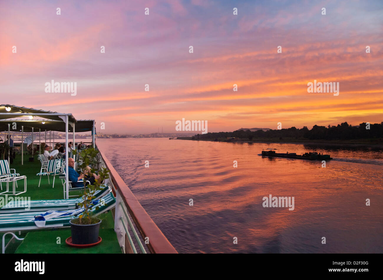 Avis de touristes de détente sur le pont supérieur d'un bateau de croisière au coucher du soleil sur le Nil au coucher du soleil l'Egypte Moyen Orient Banque D'Images
