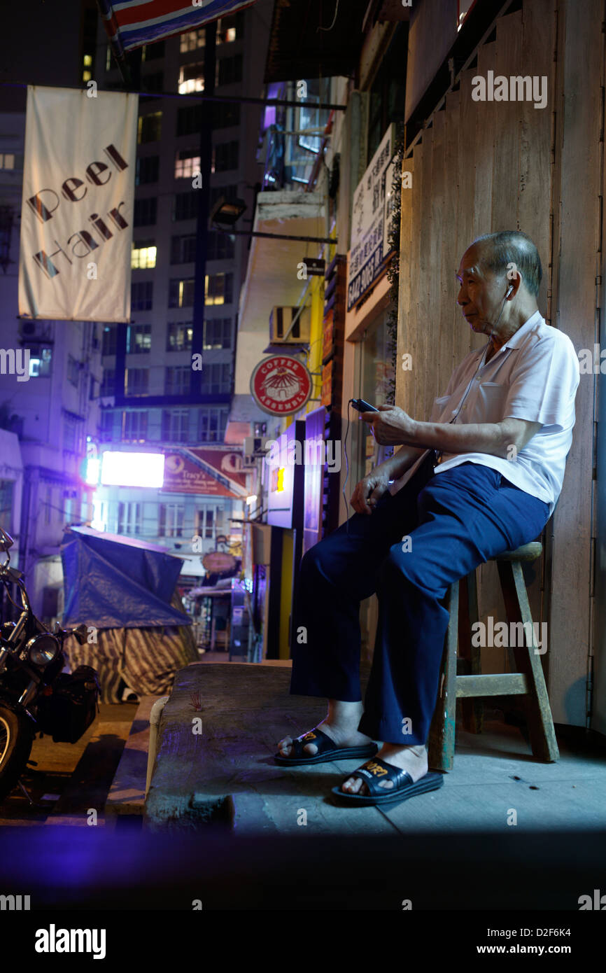 Hong Kong, Chine, un vieil homme assis dans les rues de Hong Kong et entend la musique Banque D'Images