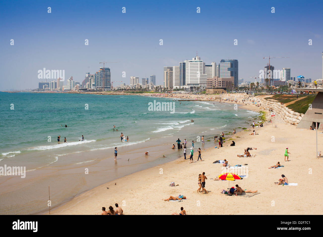 Les gens foule sur la plage de Jaffa à regarder en arrière vers l'horizon de Tel Aviv, Israël, par une chaude journée ensoleillée avec la marée. Banque D'Images