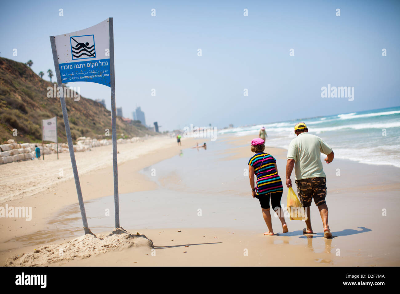 Un couple passe devant un panneau d'avertissement d'interdiction de baignade sur une plage de la mer Méditerranée en Israël. Banque D'Images