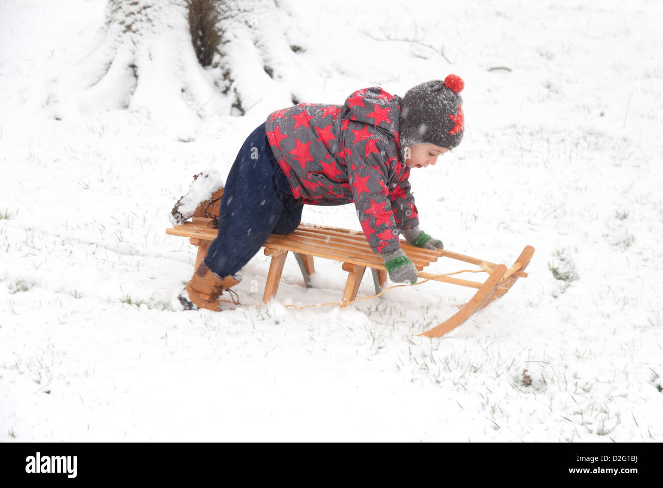 Trois ans à l'extérieur de jouer dans la neige sur un toboggan. Alresford Hampshire, Angleterre, Royaume-Uni. Banque D'Images