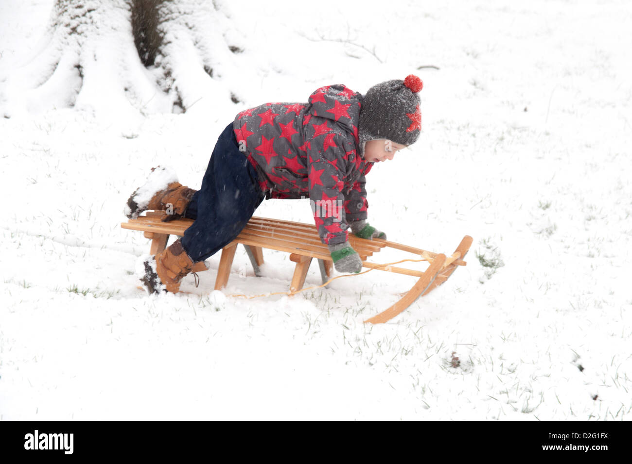 Trois ans à l'extérieur de jouer dans la neige sur un toboggan. Alresford Hampshire, Angleterre, Royaume-Uni. Banque D'Images