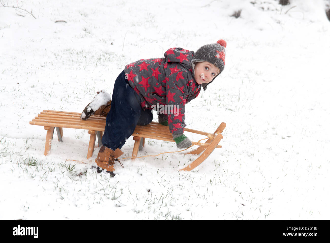 Trois ans à l'extérieur de jouer dans la neige sur un toboggan. Alresford Hampshire, Angleterre, Royaume-Uni. Banque D'Images