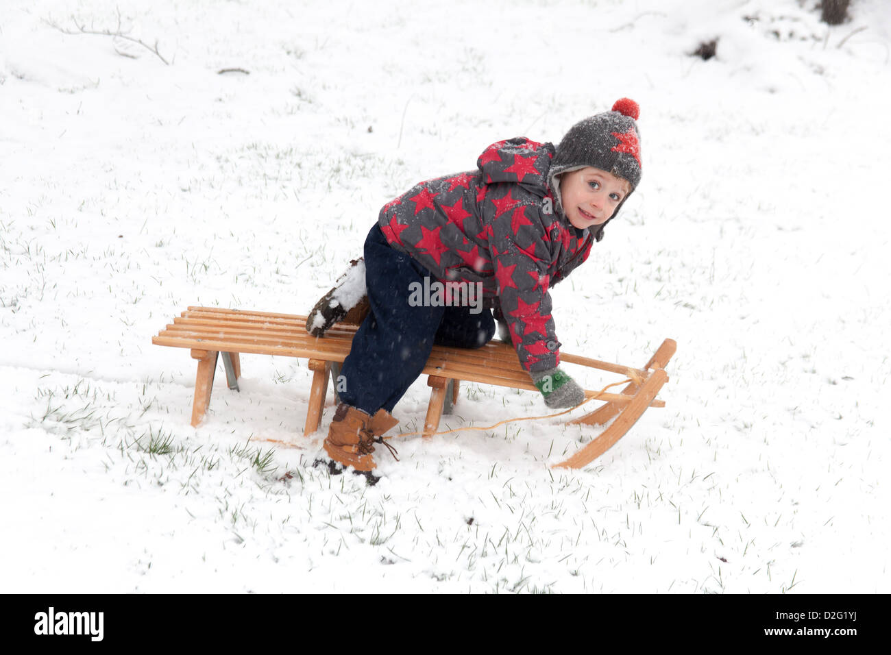 Trois ans à l'extérieur de jouer dans la neige sur un toboggan. Alresford Hampshire, Angleterre, Royaume-Uni. Banque D'Images