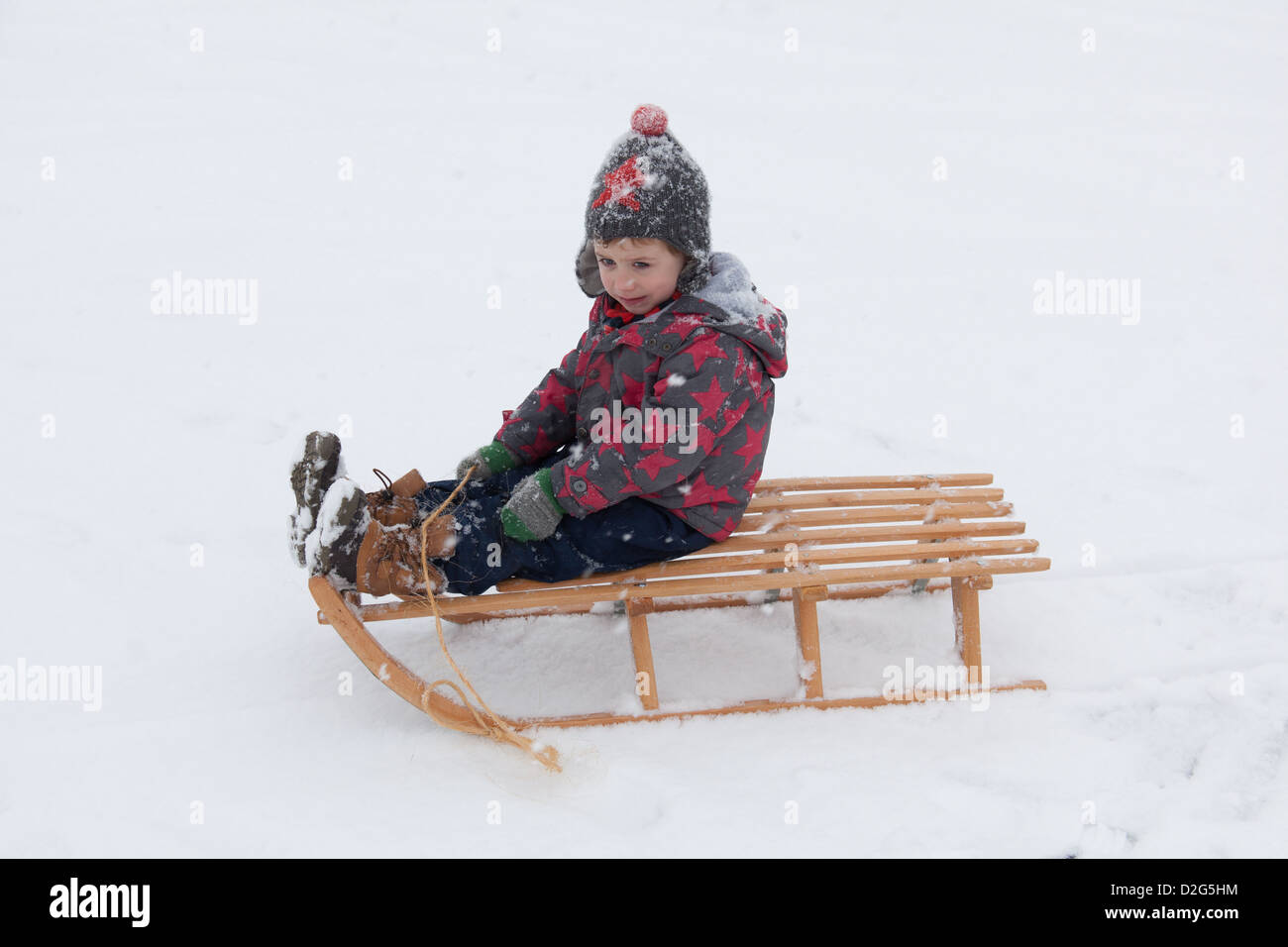 Trois ans à l'extérieur de jouer dans la neige sur un toboggan. Alresford Hampshire, Angleterre, Royaume-Uni. Banque D'Images
