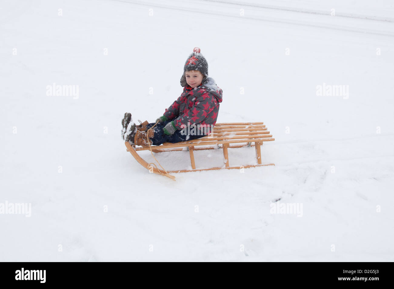 Trois ans à l'extérieur de jouer dans la neige sur un toboggan. Alresford Hampshire, Angleterre, Royaume-Uni. Banque D'Images