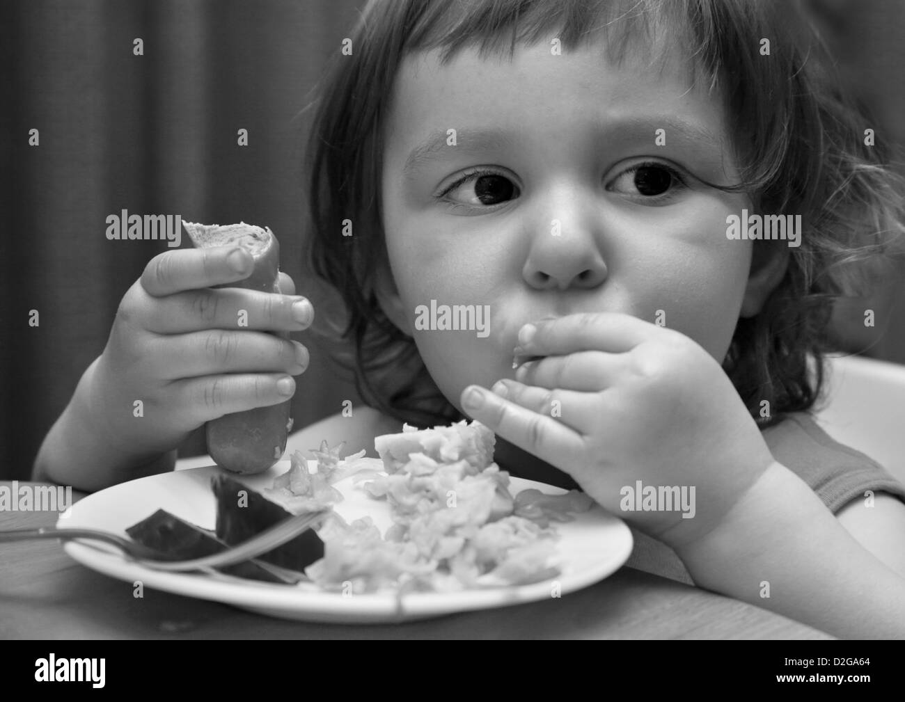 Le petit enfant mange saucisse avec macaroni. b/w Banque D'Images Le petit enfant mange saucisse avec macaroni. b/w Banque D'Images