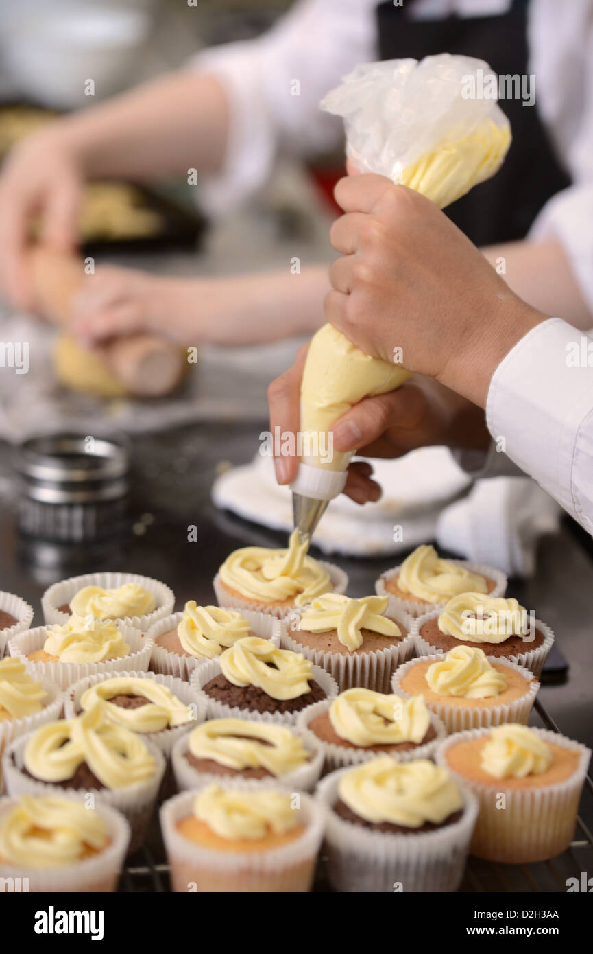 Une écolière en utilisant un sac de glace en haut cupcakes au cours d'une leçon de science alimentaire à Pates Grammar School à Cheltenham, Gloucestersh Banque D'Images