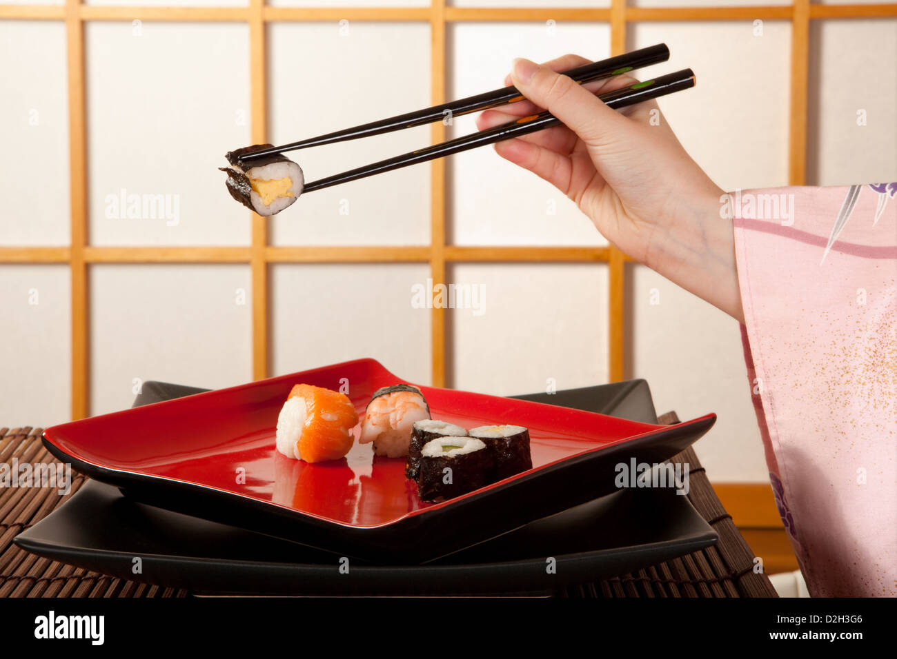 Hands holding sushi avec des baguettes en face d'une fenêtre coulissante shoji japonais Banque D'Images