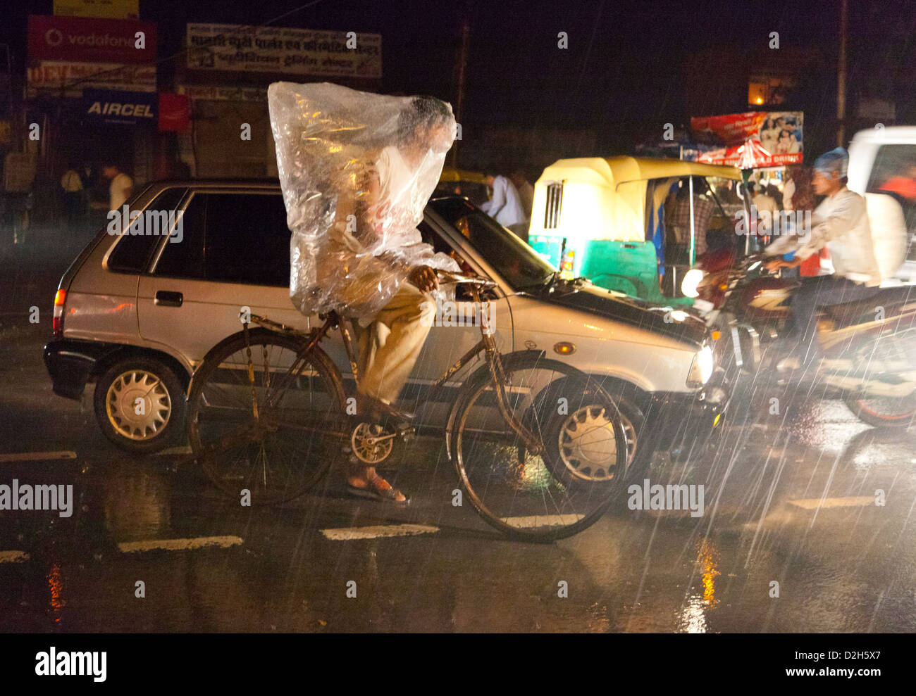 L'Inde, Uttar Pradesh, Agra man on bicycle avec sac en plastique couvrant le haut du corps dans la pluie de mousson Banque D'Images