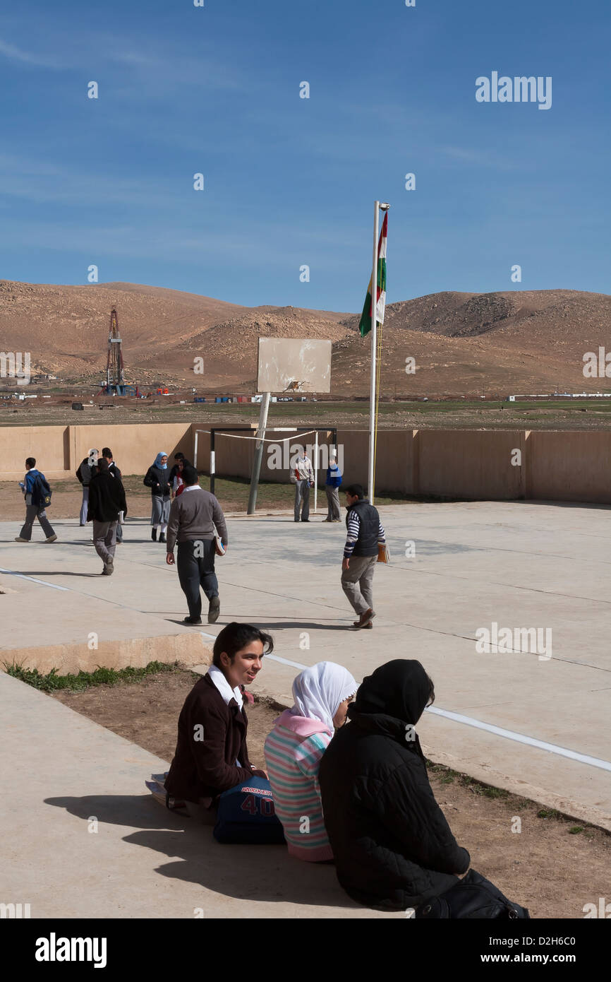 Les élèves de primaire et des jeux pour enfants à l'extérieur de l'école kurde irakienne dans le Nord de l'Iraq avec l'exploration pétrolière Rig derrière Banque D'Images