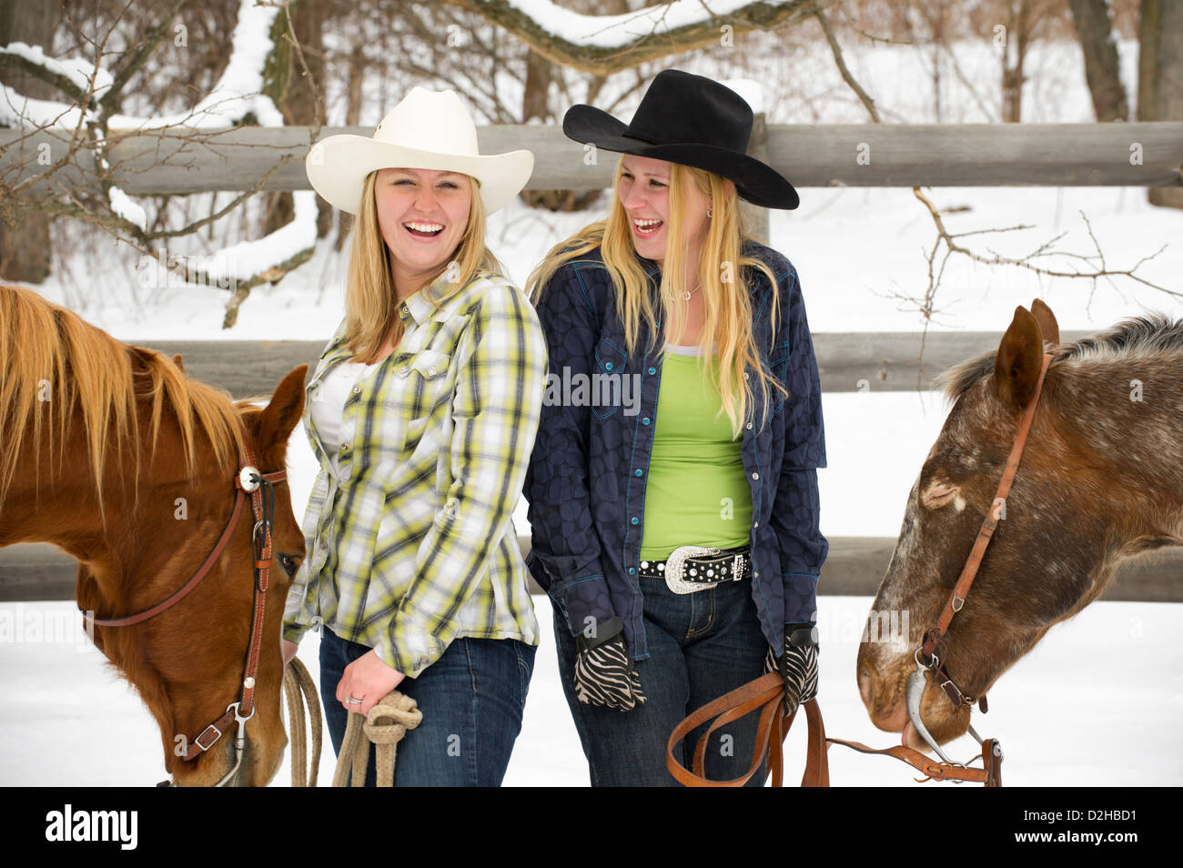 Deux cowgirls rire, plaisanter et s'amuser, debout à côté de leurs chevaux en dehors de la neige en hiver, les vêtements de style occidental. Banque D'Images