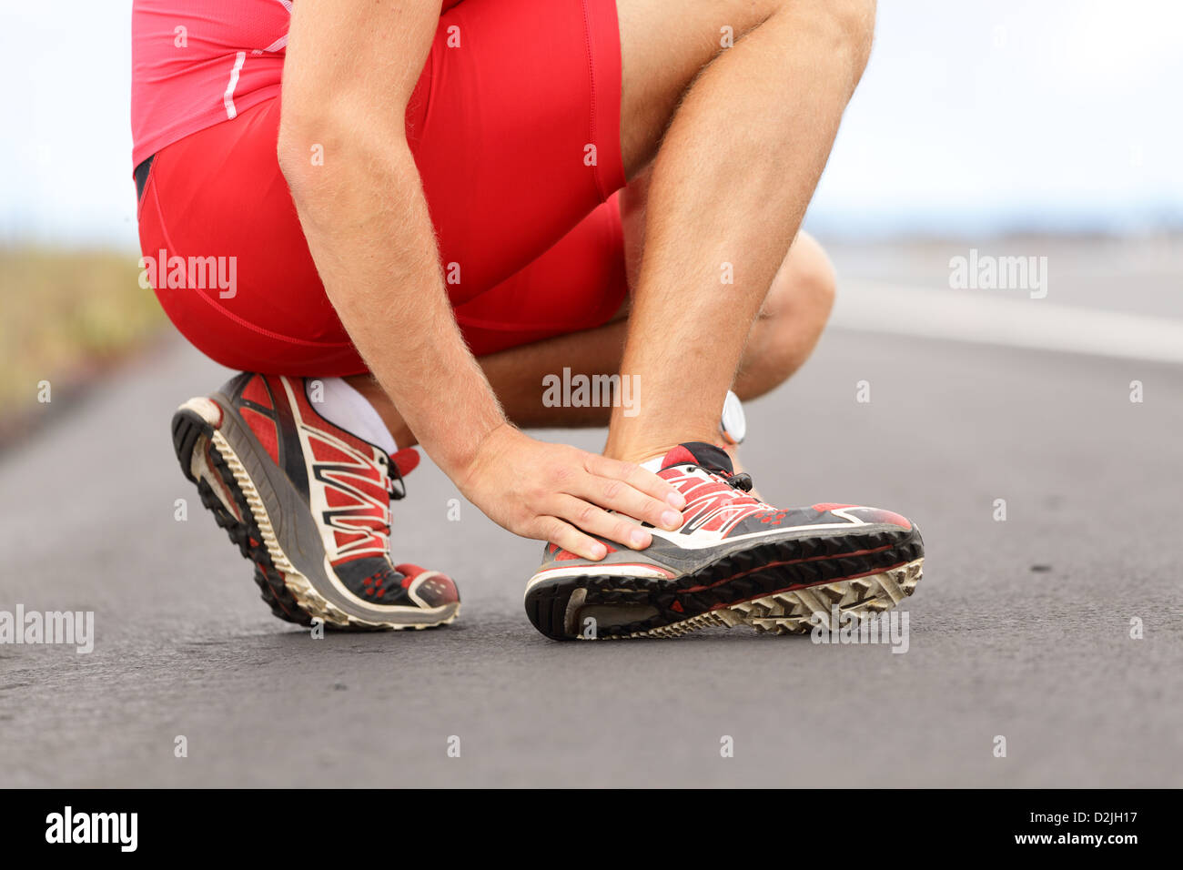 La section basse de young male runner toucher pied dans la douleur à cause de l'entorse de la cheville sur la route Banque D'Images
