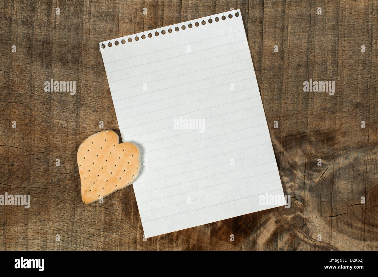 Biscuit en forme de coeur sur fond de bois et de feuilles de papier blanc Banque D'Images