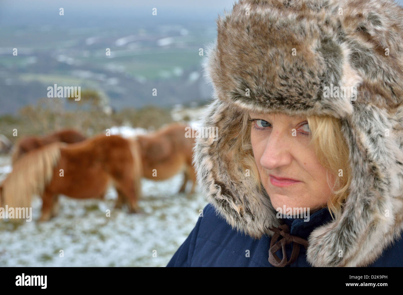 Young woman in fur hat looking at camera avec de la neige et des poneys dans l'arrière-plan Banque D'Images