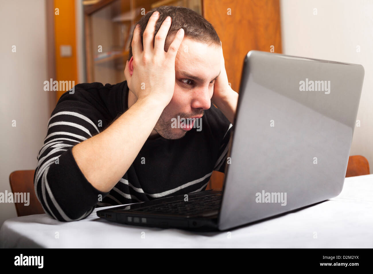 Jeune homme choqué l'aide à la recherche à l'ordinateur portable. Banque D'Images