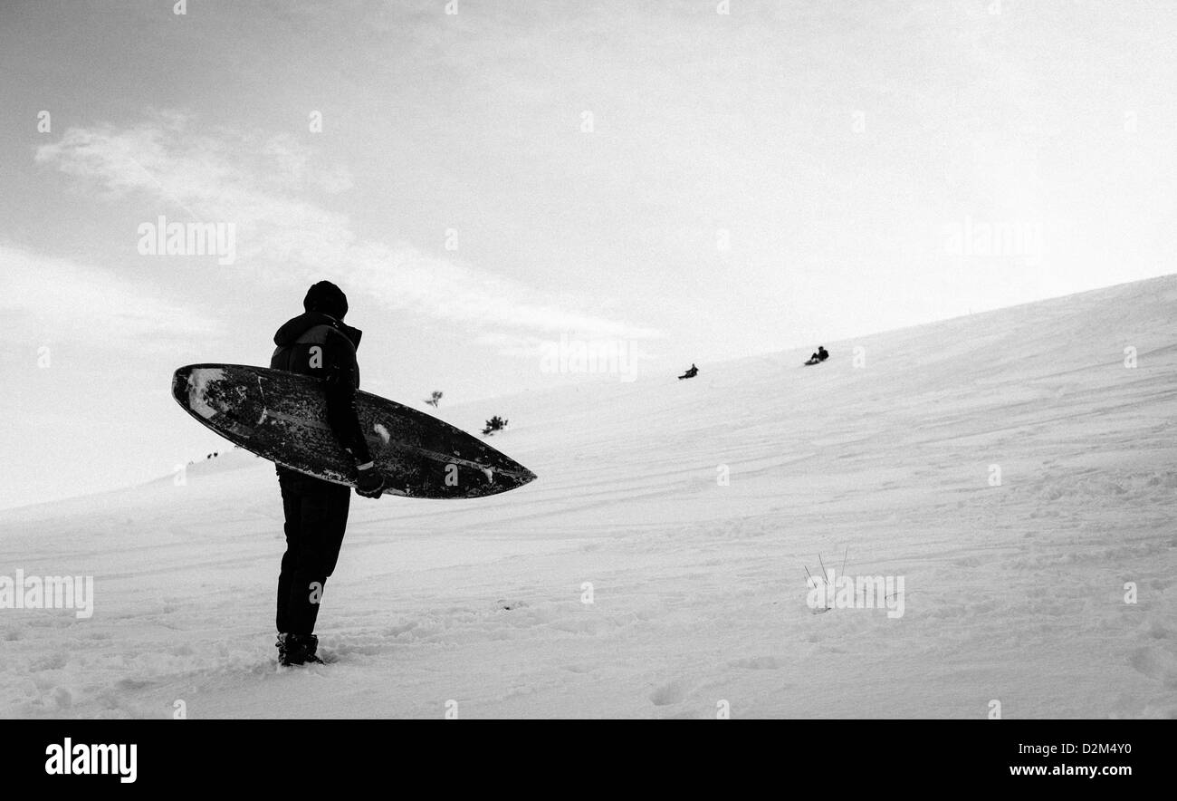 Un homme attend en bas d'une pente couverte de neige avant de tenter de monter une planche de surf au bas de la colline. Banque D'Images
