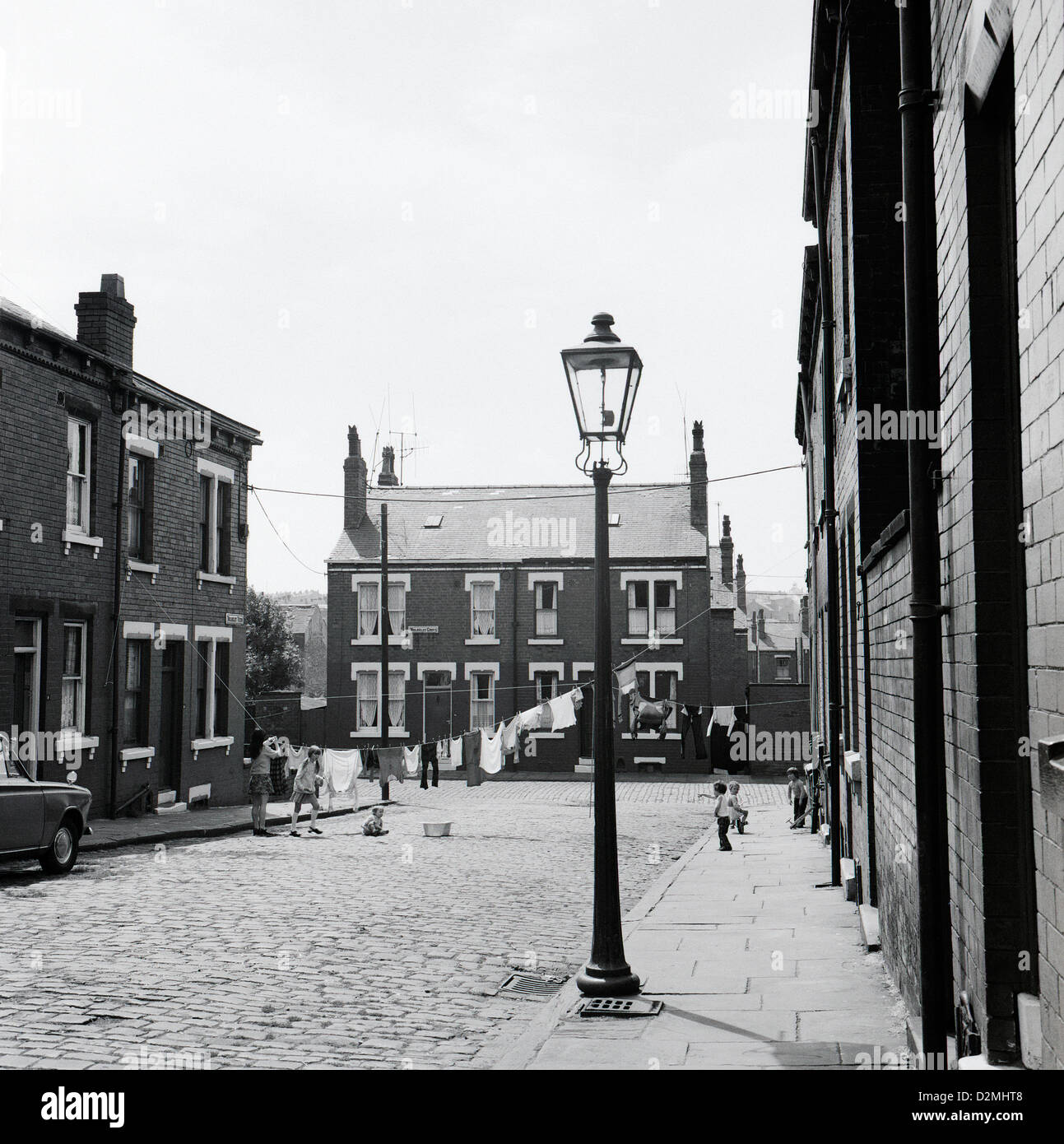 Lampe de rue au gaz et la mère pendait la blanchisserie sur une ligne de lavage dans une vieille rue pavée avec des maisons victoriennes en terrasse et les enfants jouant des jeux en 1970s années 70 70s Wolseley Grove Leeds Angleterre Royaume-Uni Grande-Bretagne 1974 KATHY DEWITT Banque D'Images