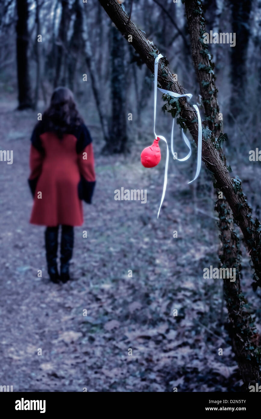 Un vieux ballon rouge suspendu à une branche, à une distance d'une femme dans un manteau rouge Banque D'Images
