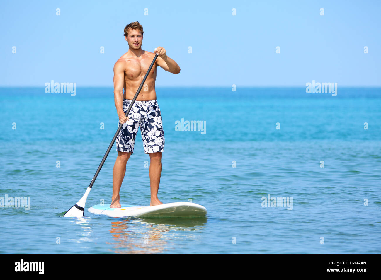 Young Caucasian man standing heureux sur la pagaie surfboard sur plage hawaïenne sur les vacances d'été Banque D'Images