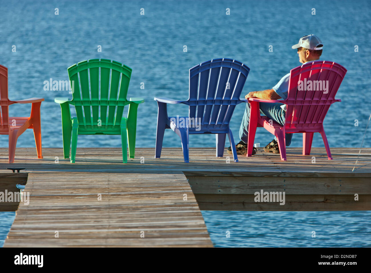 Senior male assis une chaise en plastique rouge, quai de pêche. Banque D'Images