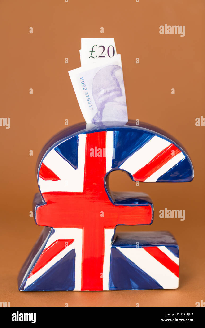 Une tirelire en forme de symbole de devise livre sterling arborant le drapeau britannique Union Jack étant remplis d'argent Banque D'Images