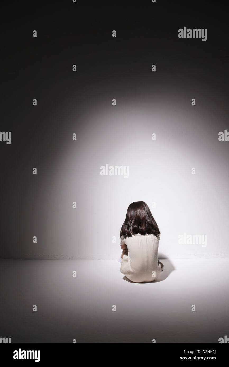 Triste jeune fille en robe blanche assise sur le sol contre le mur Banque D'Images